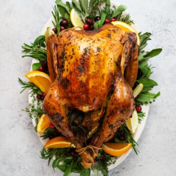 whole thanksgiving turkey on a platter with orange wedges and greens