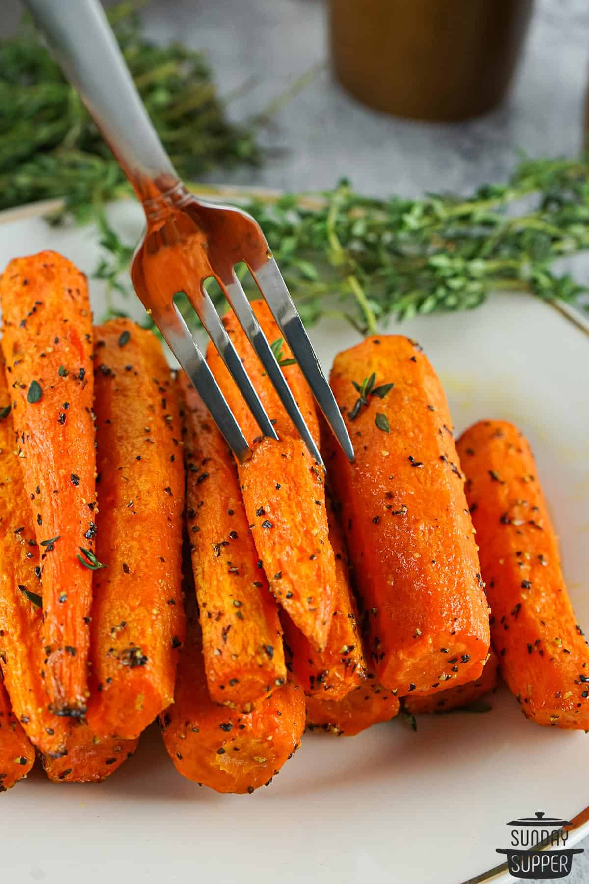 a fork taking an air fried carrot from a plate of carrots