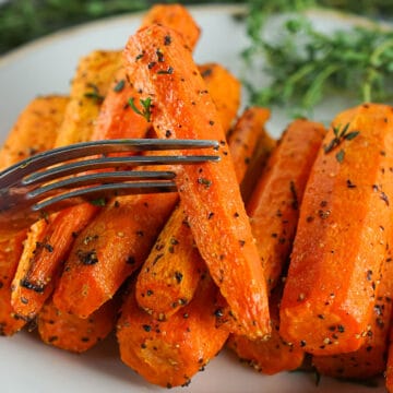 a fork with an air fried carrot over a plate of stacked carrots