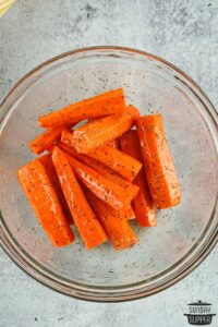 carrots coated in olive oil and seasonings in a mixing bowl