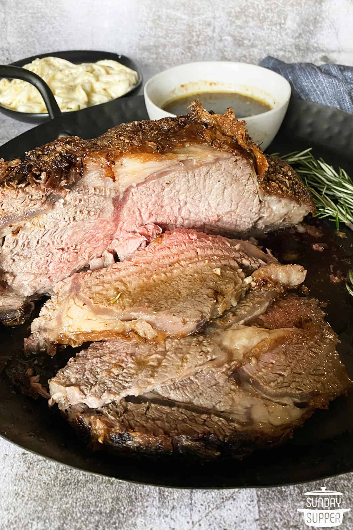 sliced air fryer prime rib on a black platter with mashed potatoes and gravy in two separate bowls