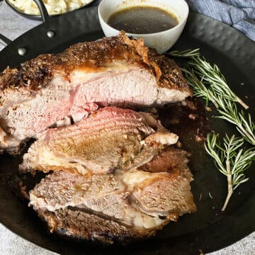a black platter of air fryer prime rib, sliced, next to herbs and gravy