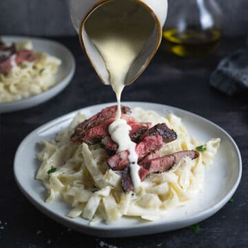 alfredo sauce being poured on a plate of fettuccine with steak