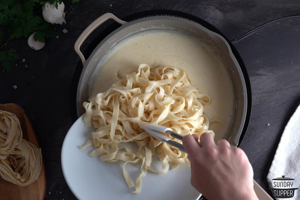 cooked fettuccine being added to the pot of sauce