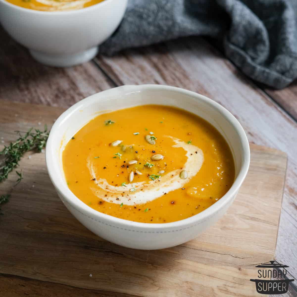 a bowl of butternut squash soup on a wood cutting board