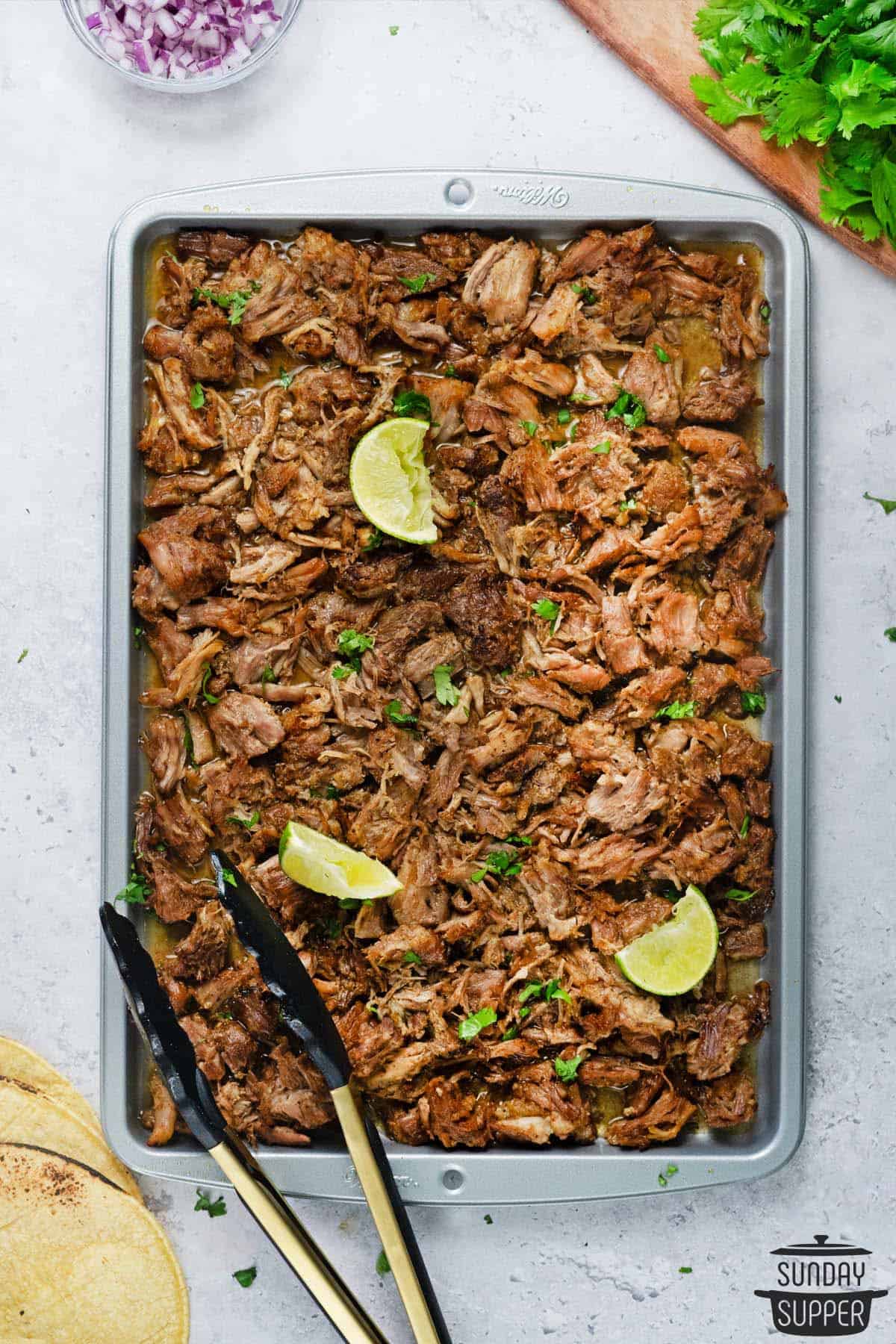 A big pan of baked carnitas with lime slices