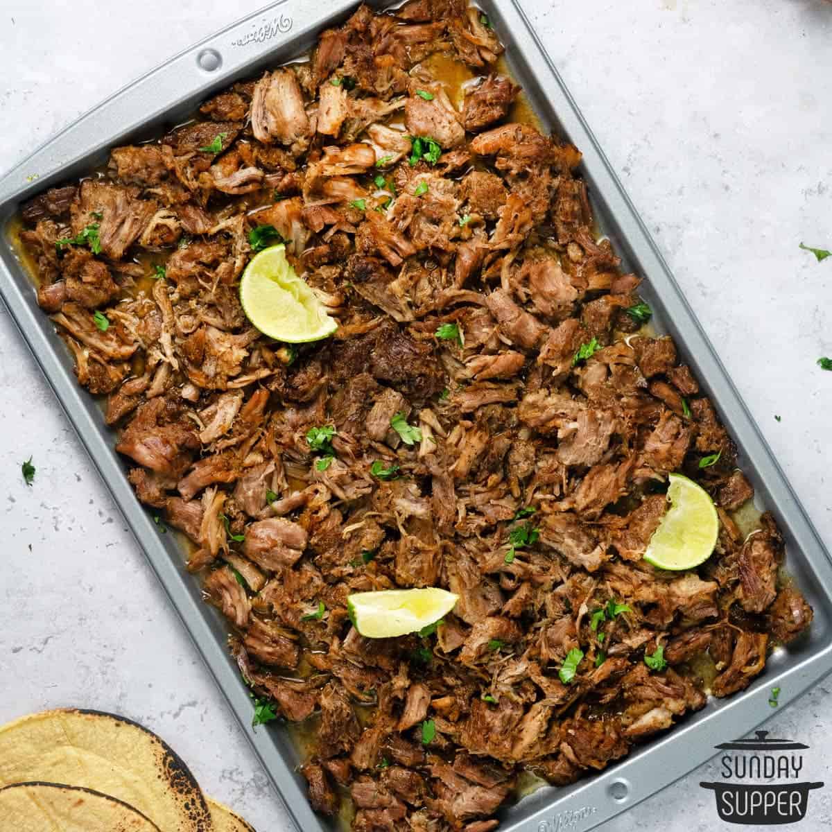 a completed pan of carnitas with lime