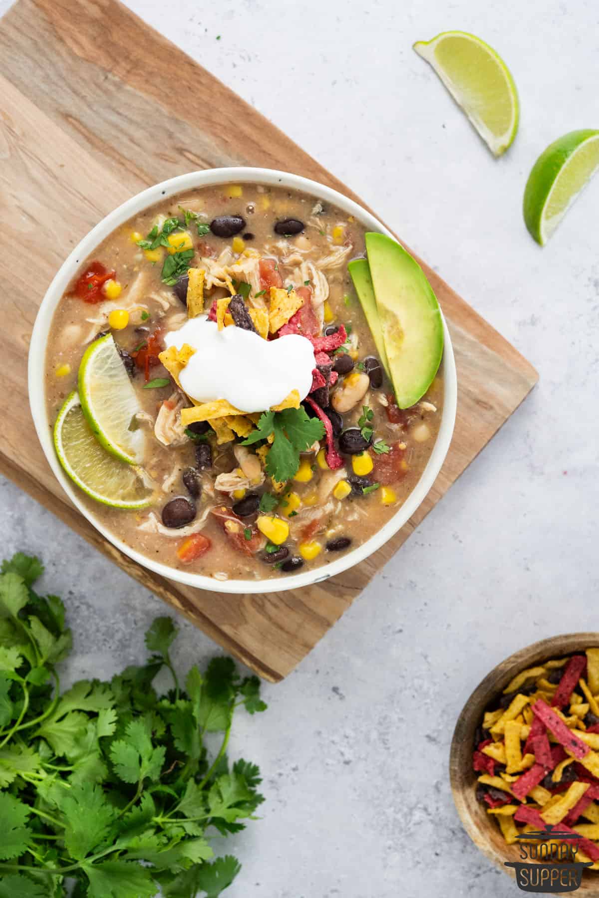 Chick-fil-A Chicken Tortilla Soup added to a bowl with avocado slices and lime wedges next to a bowl of tortilla strips