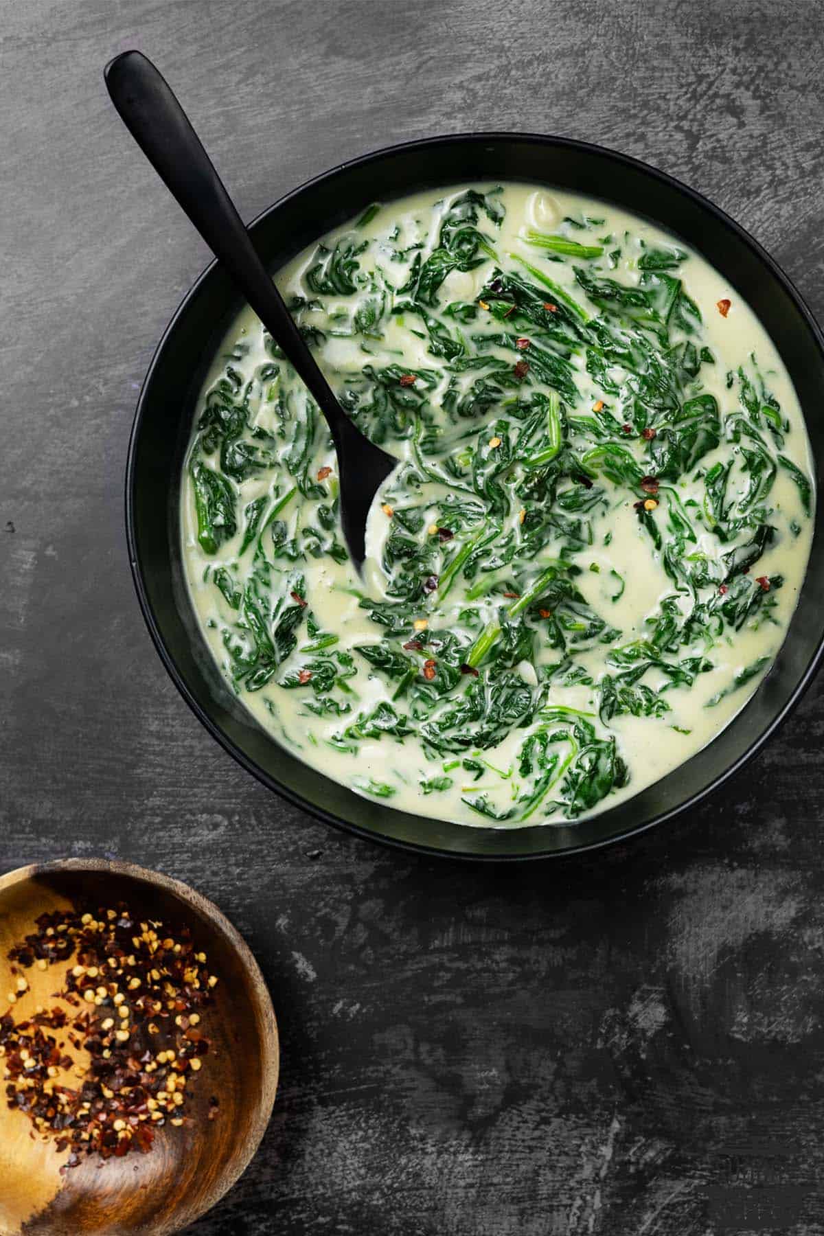 creamed spinach in a black bowl with a black spoon