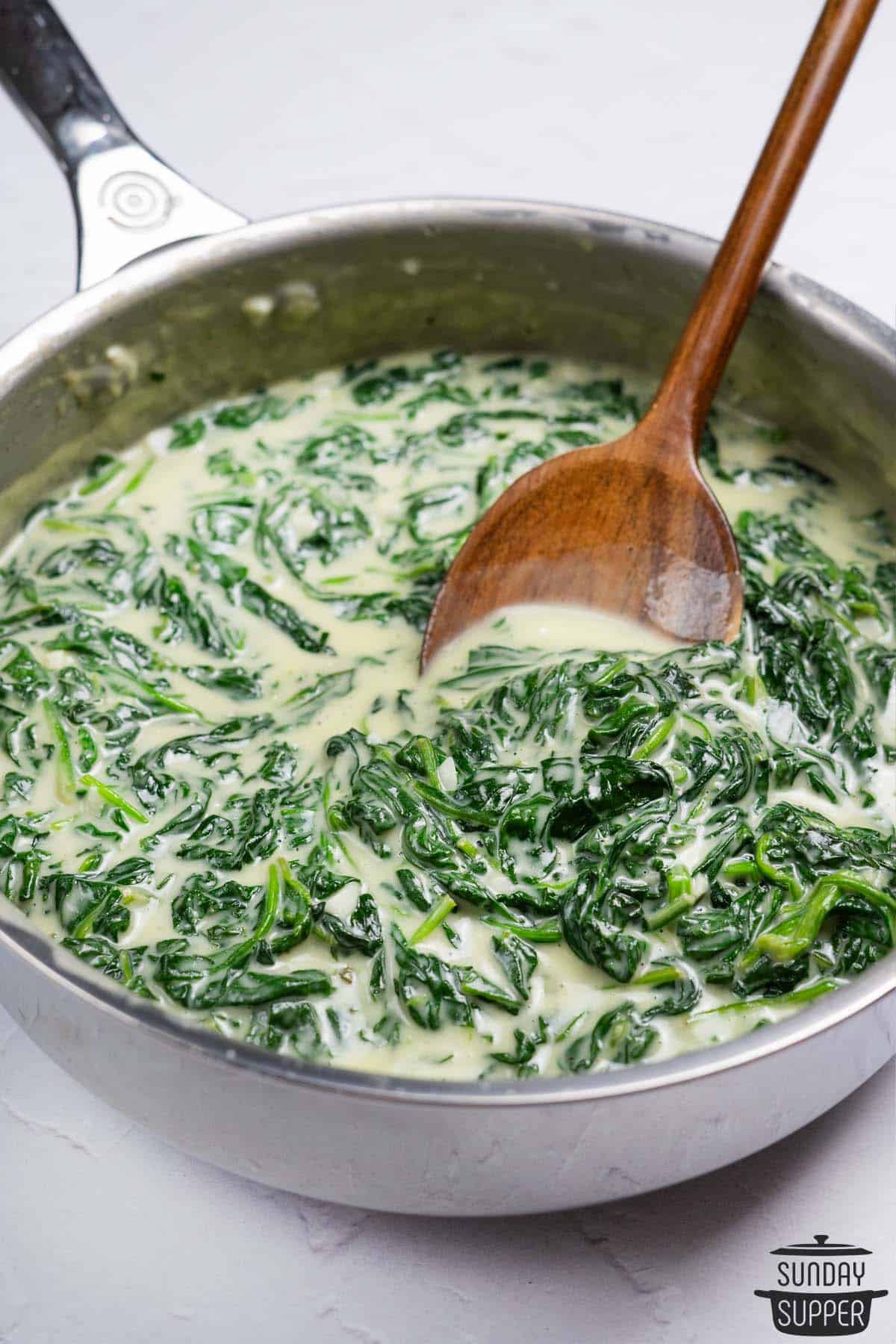 creamed spinach in a shallow pot with a wooden spoon