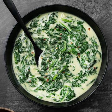 creamed spinach in a black bowl with a black spoon, seasoned with red pepper flakes