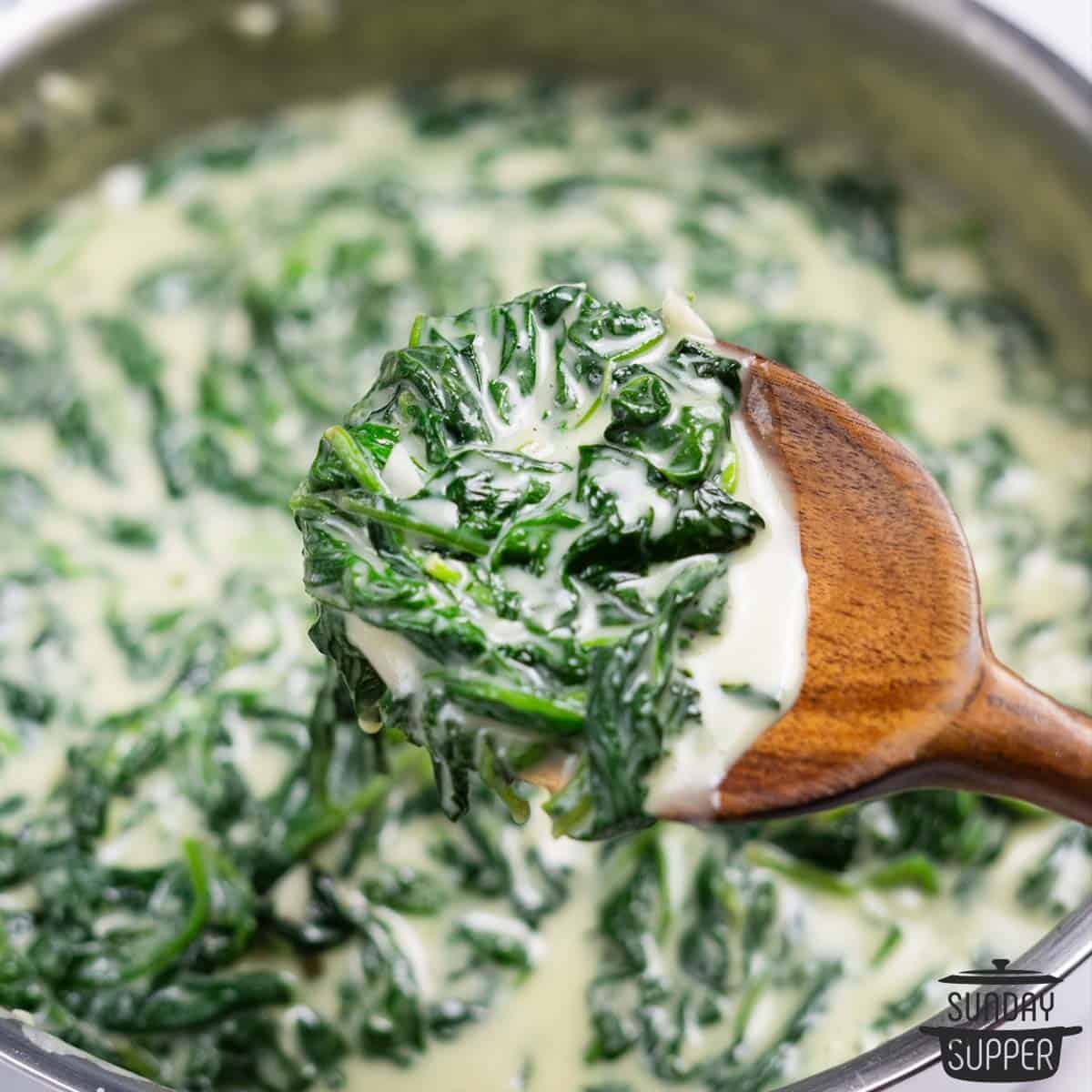 creamed spinach on a wooden spoon over a pan