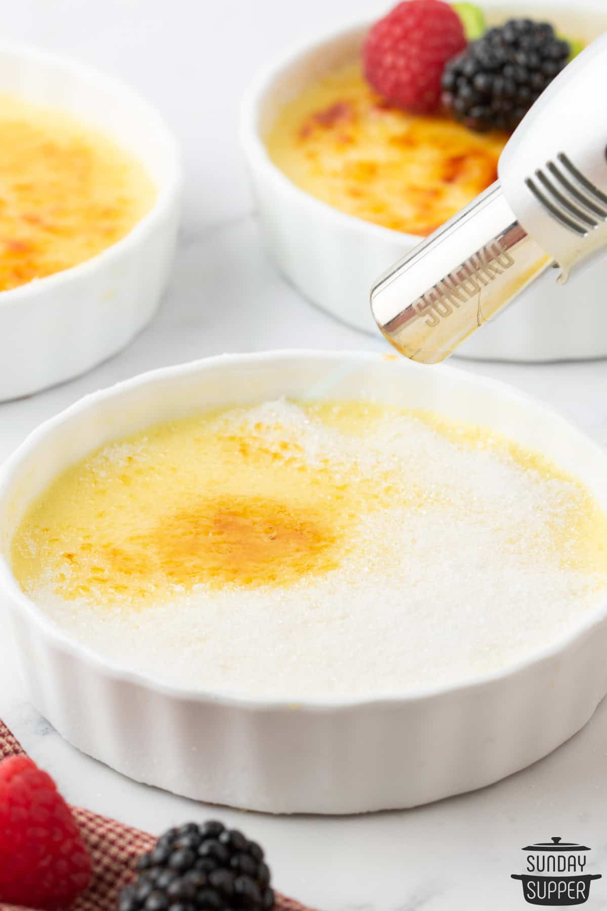 using a kitchen torch to caramelize the sugar coating on the creme brulee