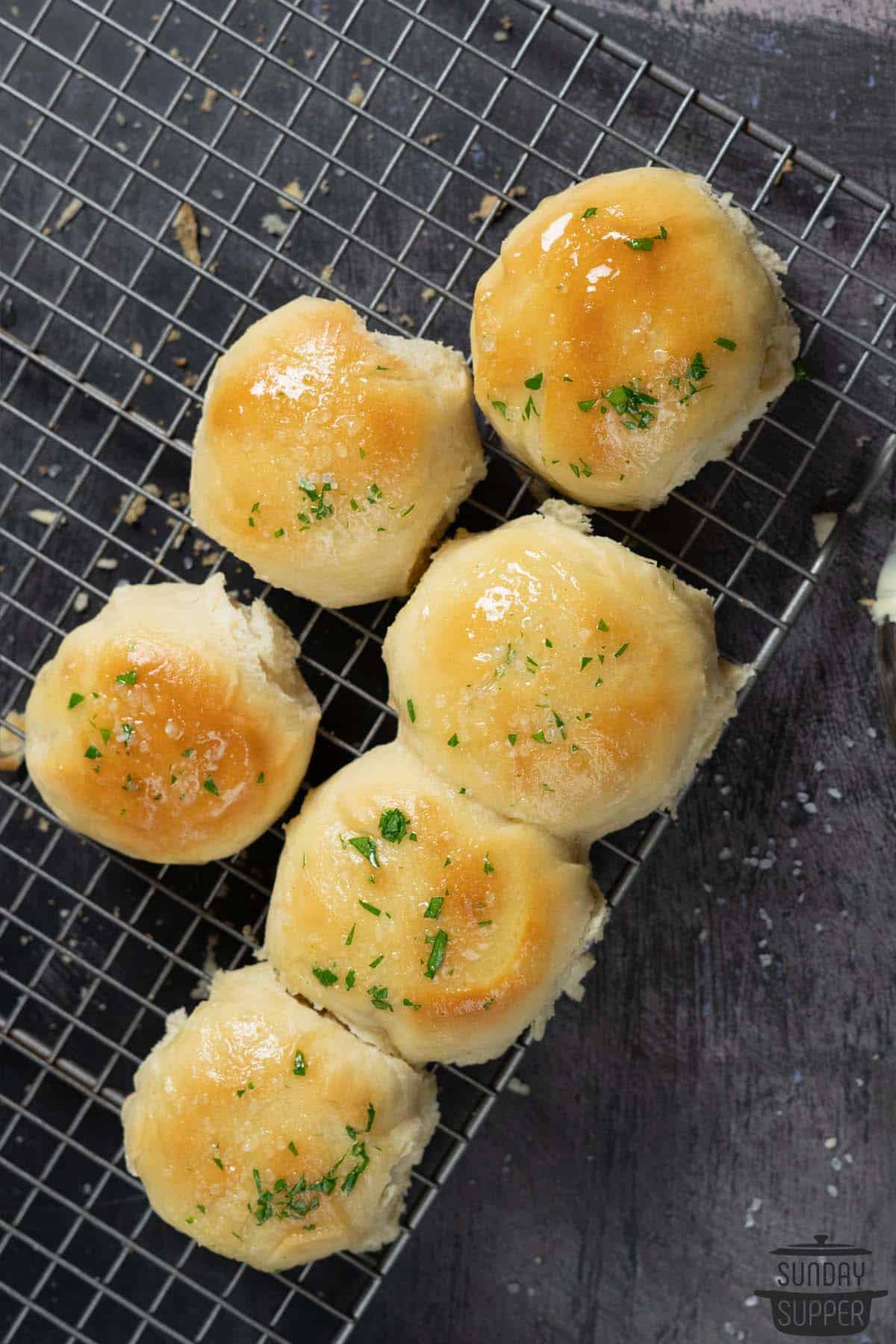 six quick dinner rolls on a cooling rack, brushed with garlic butter