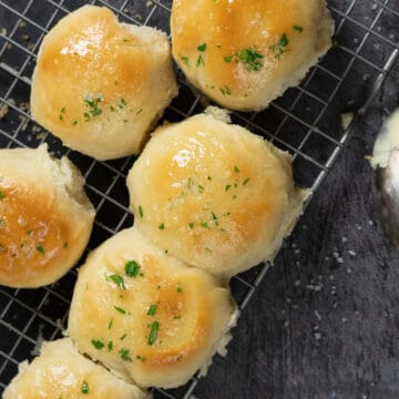 six quick dinner rolls coated with garlic butter on a cooling rack