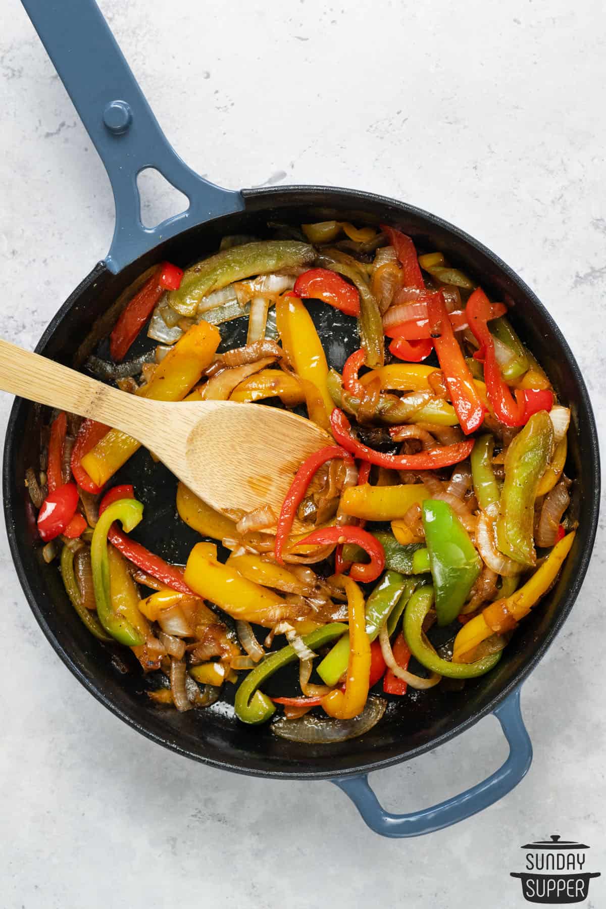 peppers and onions cooked in a skillet with a wooden spoon