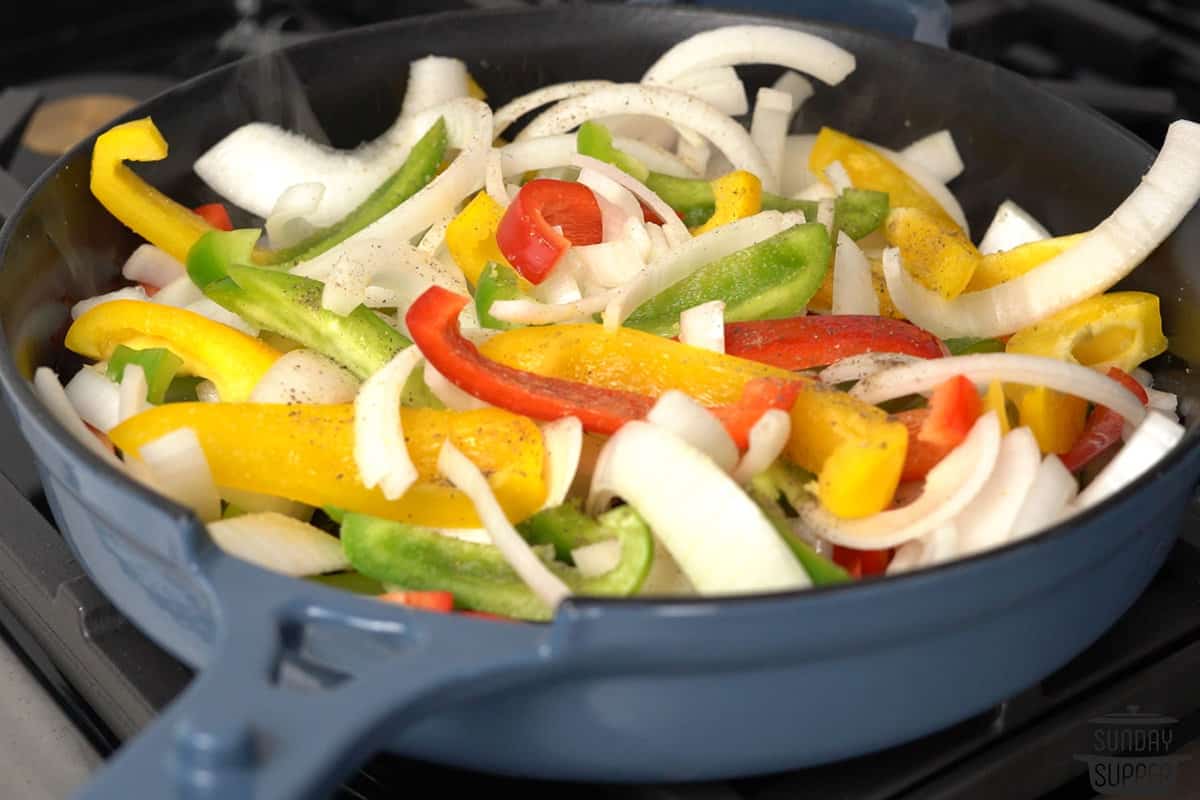 adding peppers and onions to a skillet with seasoning