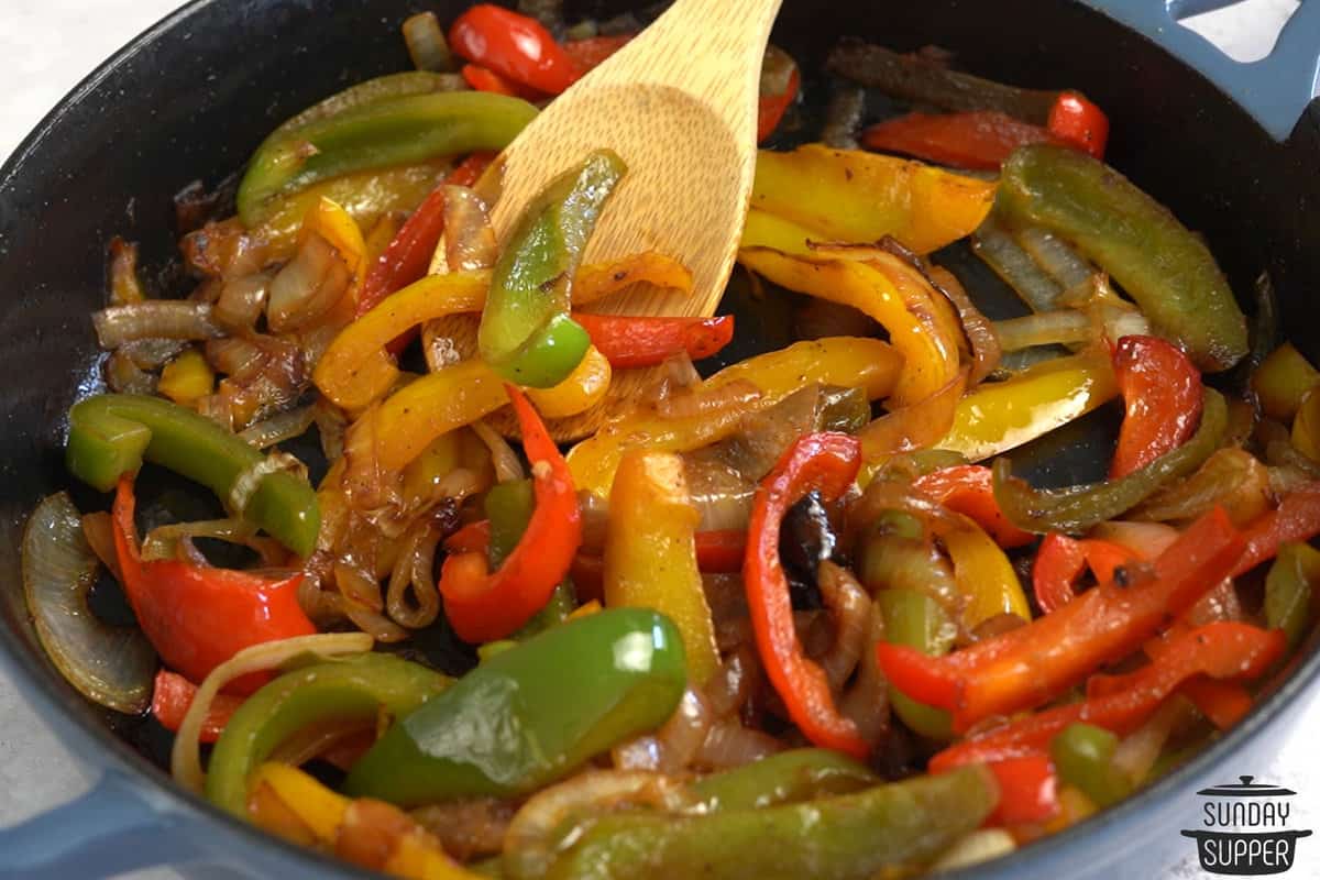 sauteed peppers and onions in a skillet with a wooden spoon, ready to eat