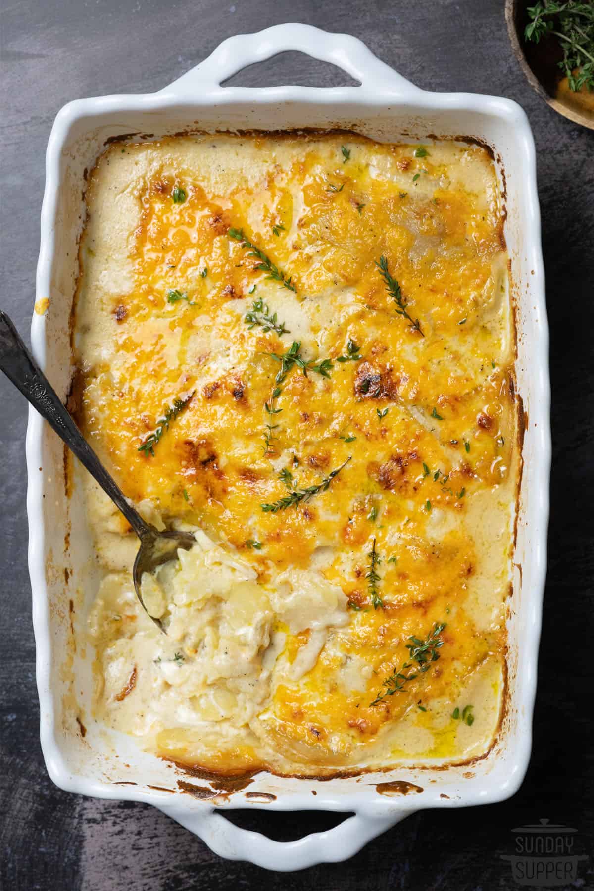 scalloped potatoes in a white casserole dish with a spoon inside