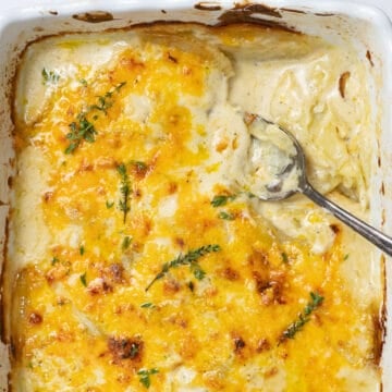 close up of scalloped potatoes in a white dish with a spoon inside