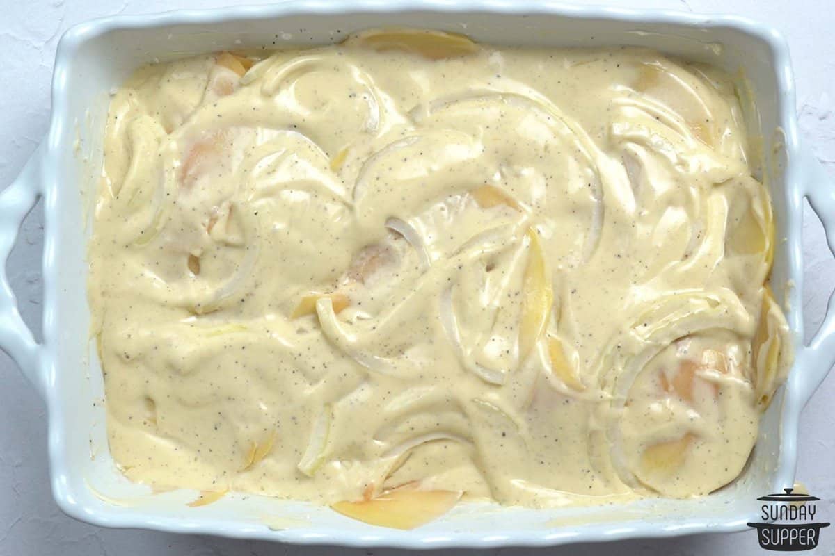 adding cheese sauce on top of sliced potatoes in a casserole dish