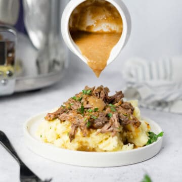 beef gravy pouring over a plate of mashed potatoes and chuck roast