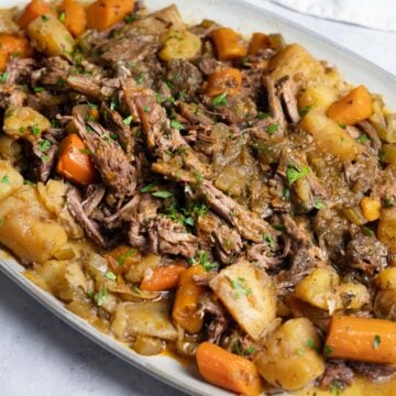 slow cooker chuck roast shredded over potatoes and carrots on a white platter