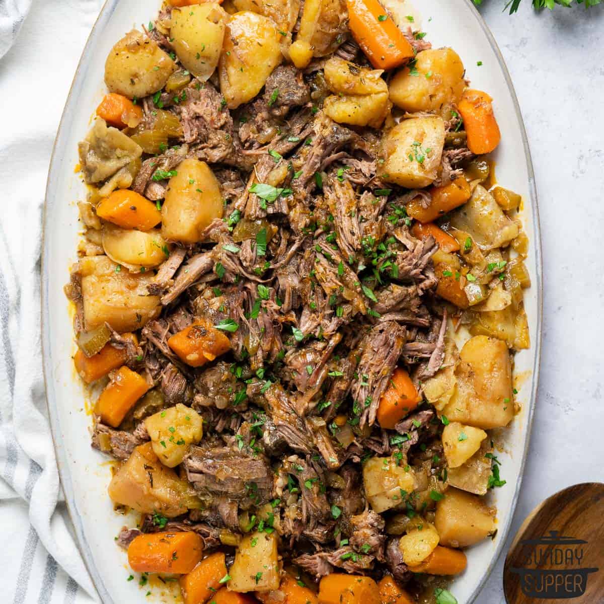 slow cooker chuck roast with potatoes and carrots on a white platter