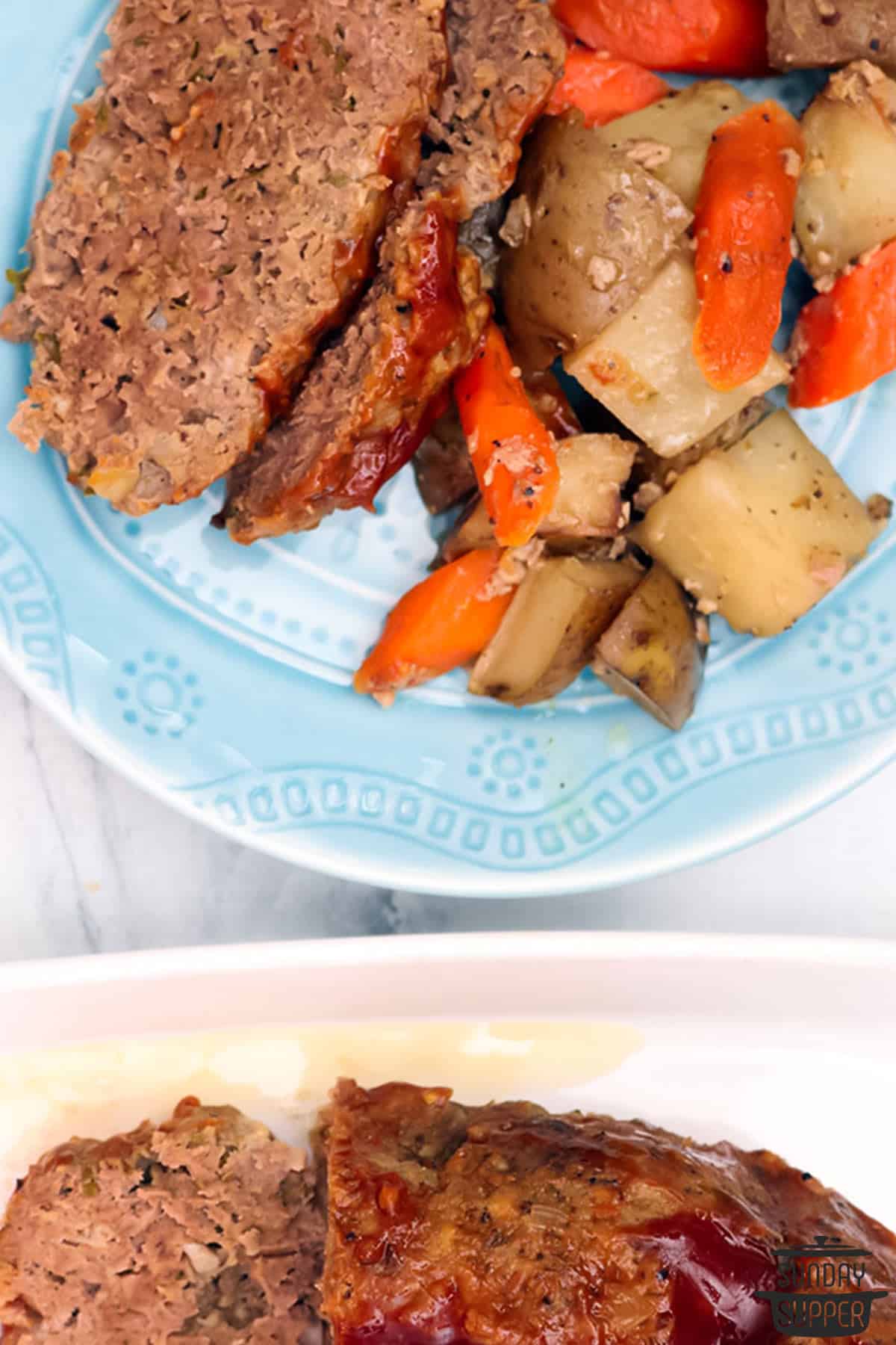 a plate of sliced meatloaf and vegetables next to a serving platter of meatloaf