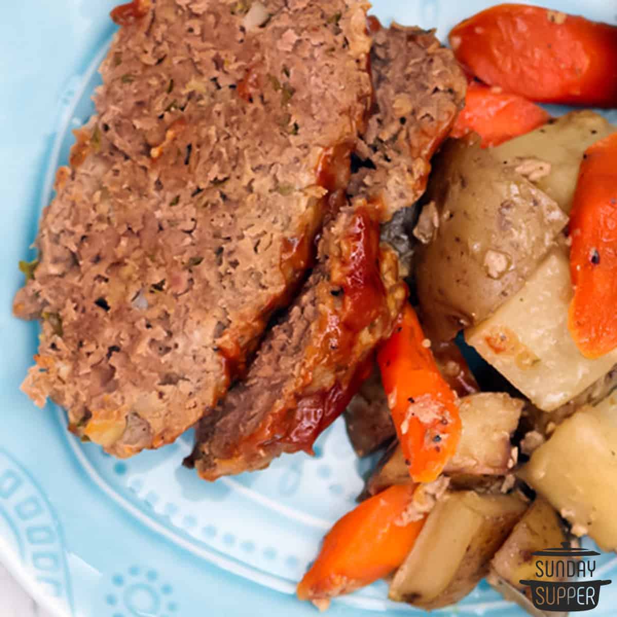a closeup of two slices of meatloaf and slow cooked vegetables on a plate