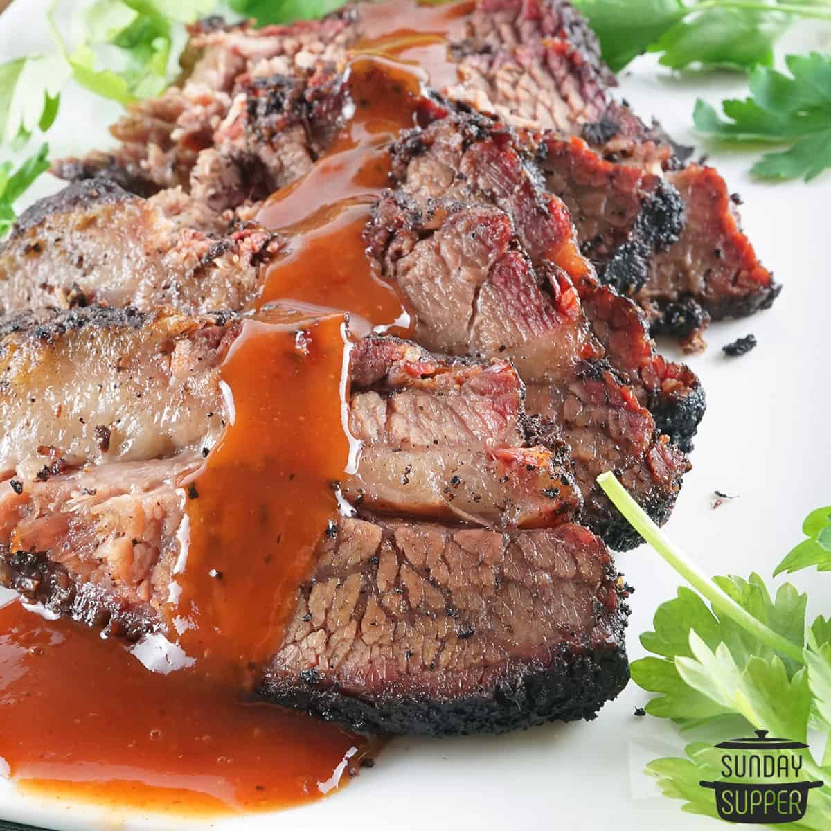 sliced beef brisket on a plate with sauce poured over top