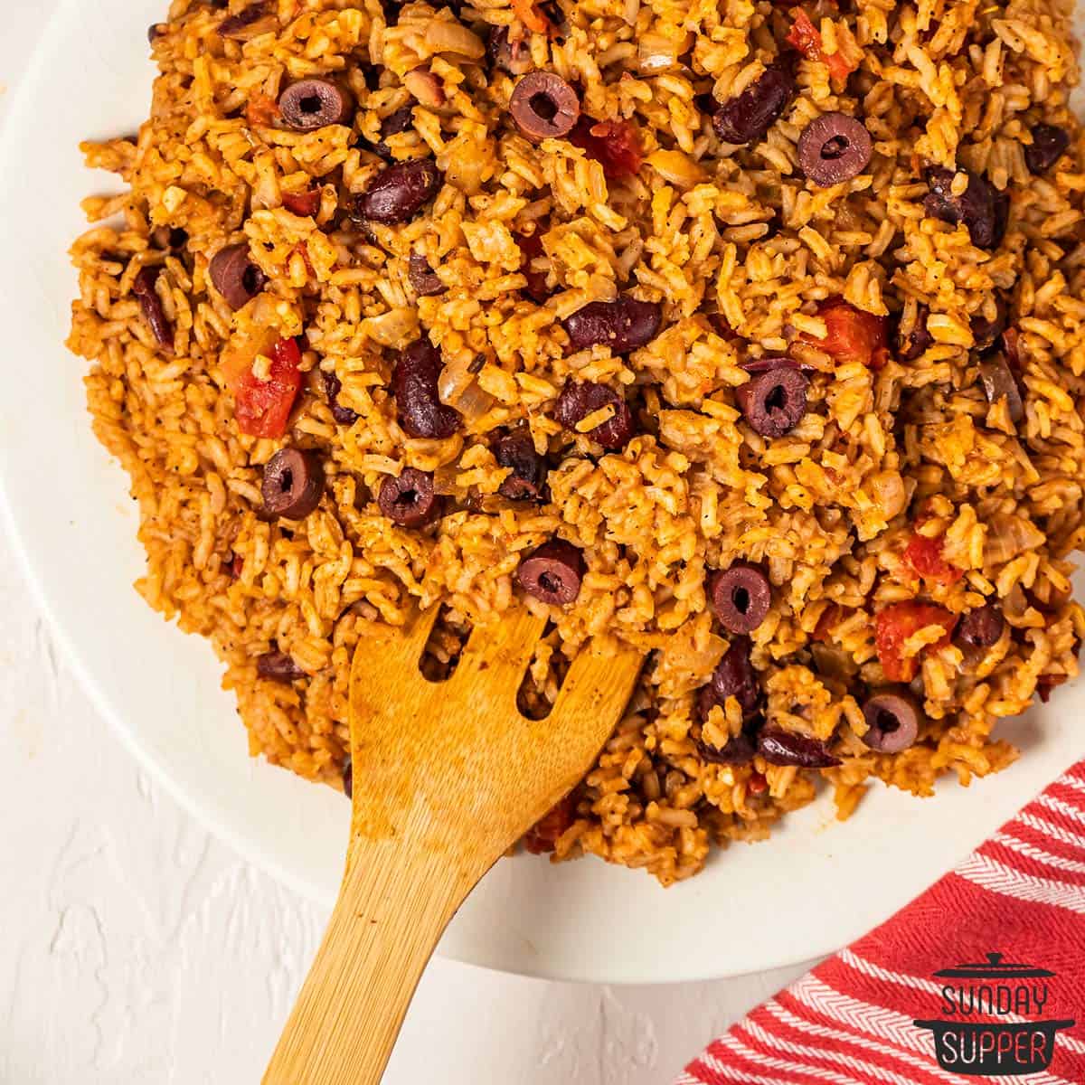 a wooden spoon digging into a plate of spanish rice and beans