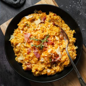 sweet potato risotto in a black bowl with a spoon inside