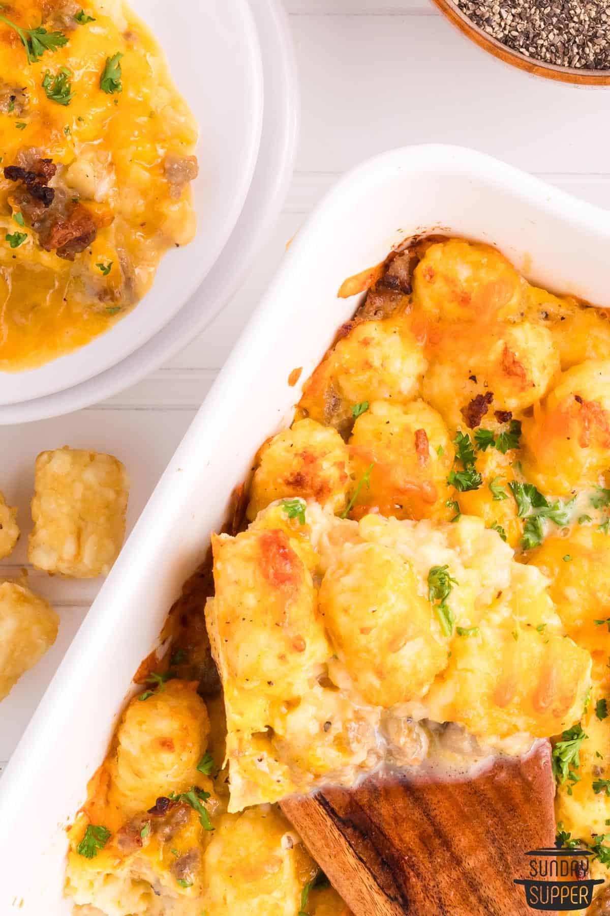 a wooden spoon full of tater tot breakfast bake over a casserole dish