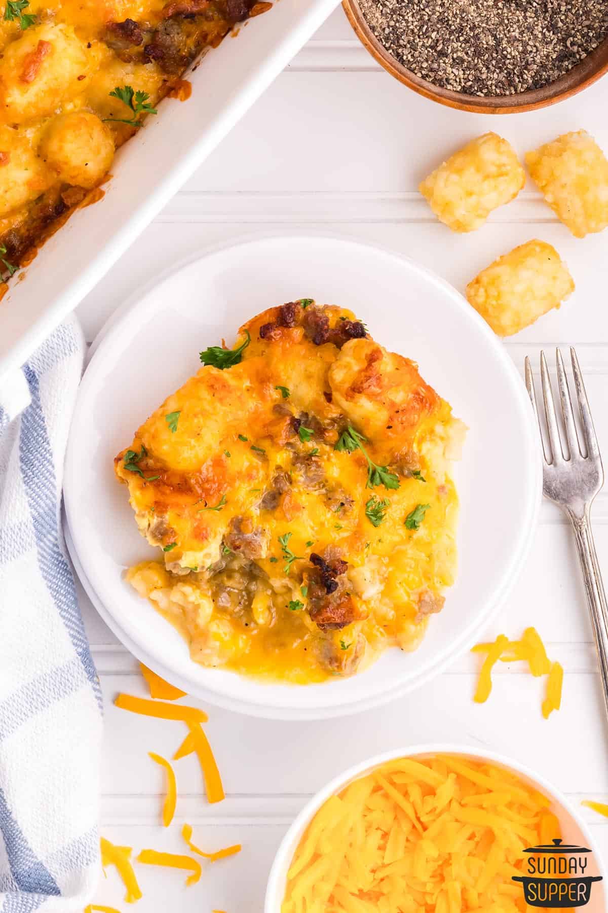 a plate of tater tot casserole with more cheese, pepper, and casserole on the side