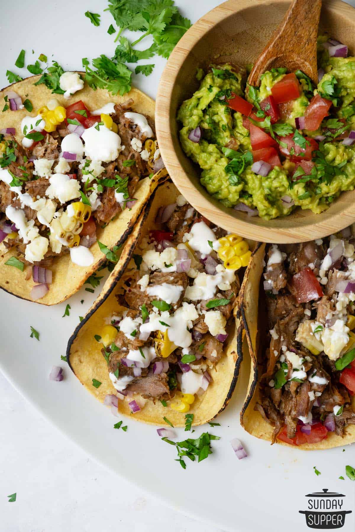 three carnitas tacos on a plate with a bowl of guacamole