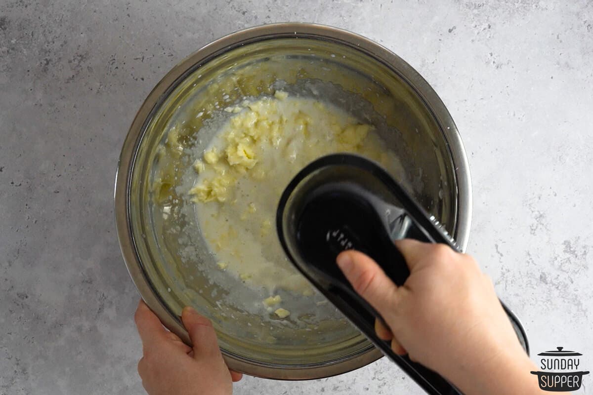 butter, milk, and sugar being creamed in a bowl with a hand mixer