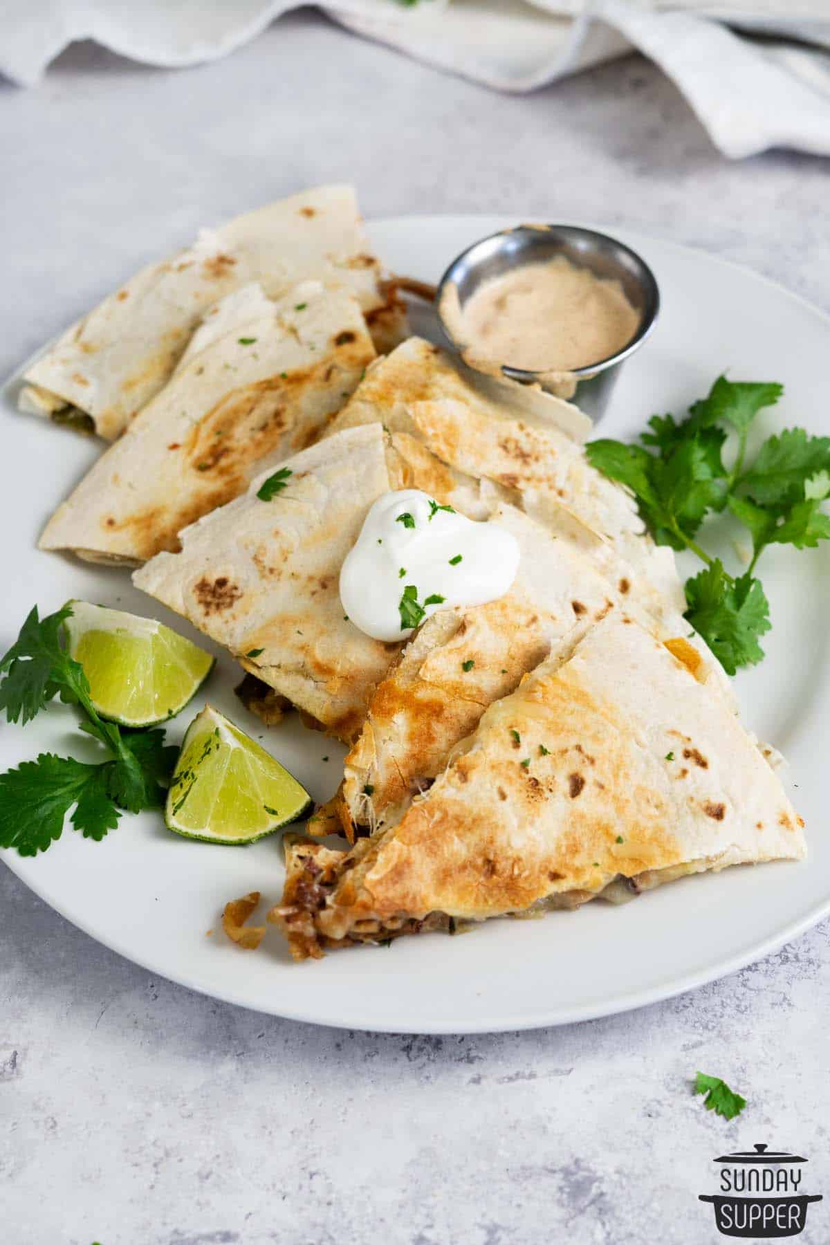 a plate of sliced pork quesadillas with dipping sauce and cilantro