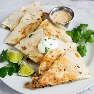 sliced quesadillas on a plate with extra lime and cilantro