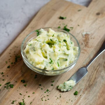 garlic butter in a glass bowl with parsley and a butter knife