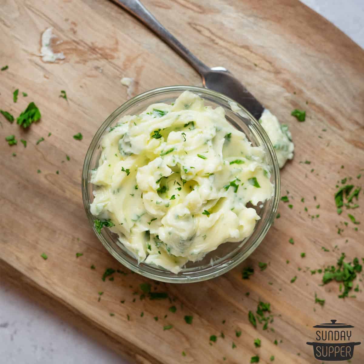 garlic butter in a bowl with a butter knife and parsley on a cutting board