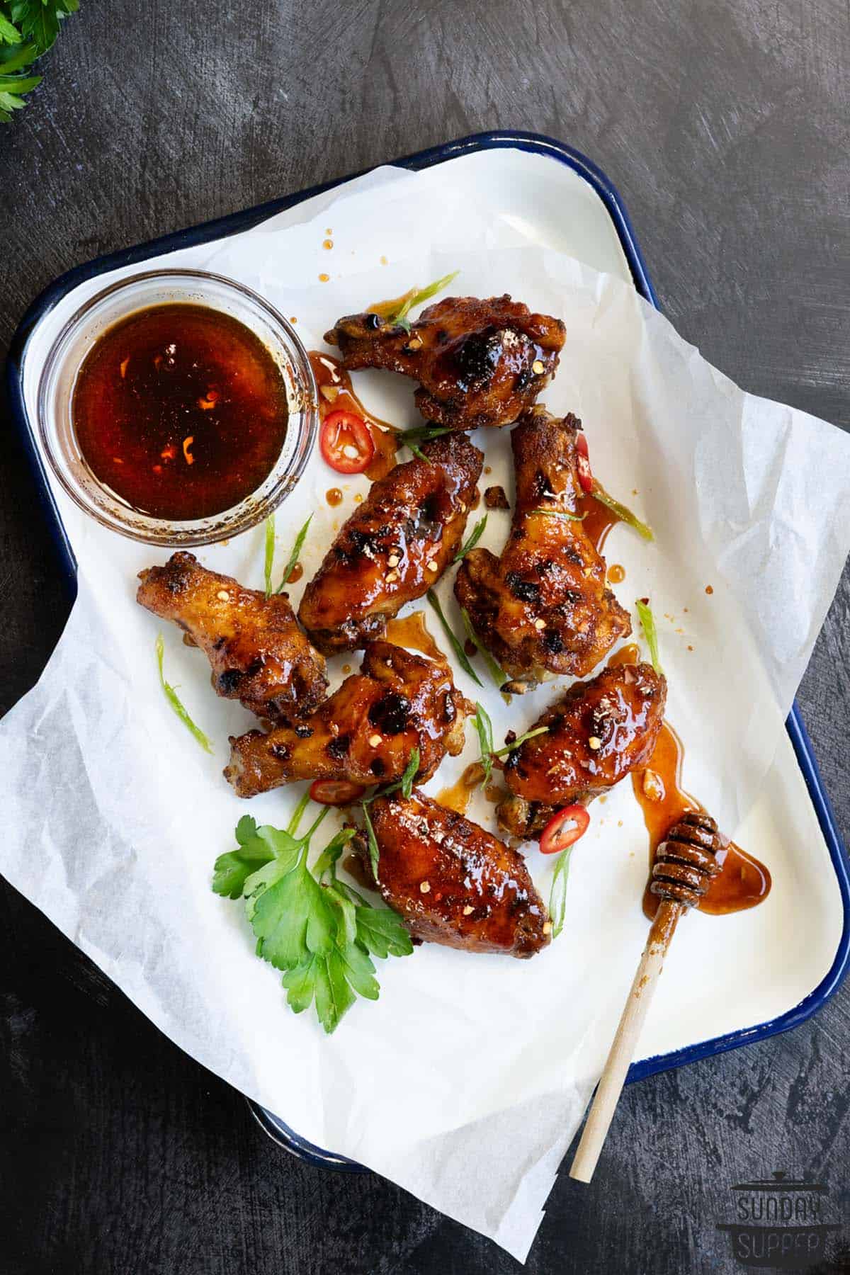 Instant pot chicken wings on a serving tray with a honey stirring stick and honey sriracha sauce in a bowl