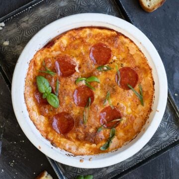 pizza dip inside of a white baking dish with fresh herbs on top