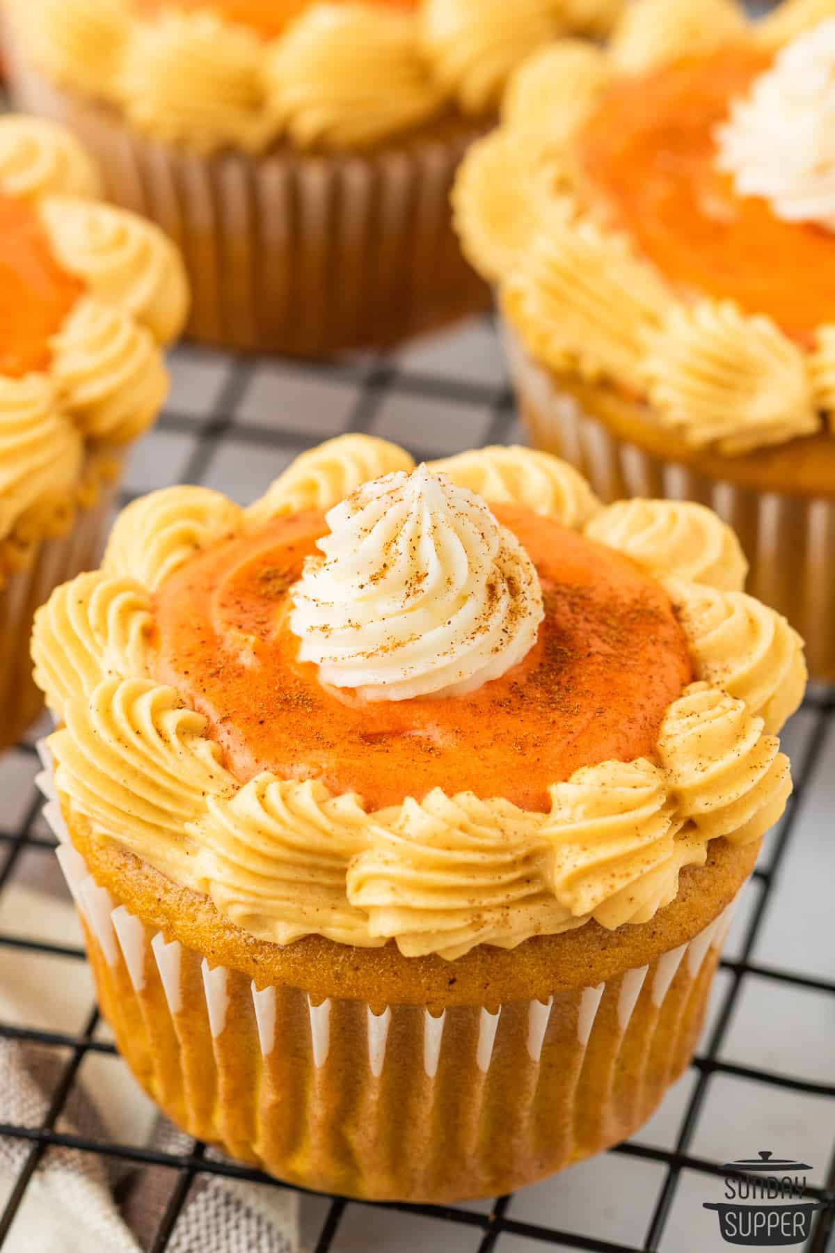 pumpkin cupcakes on a cooling rack with frosting