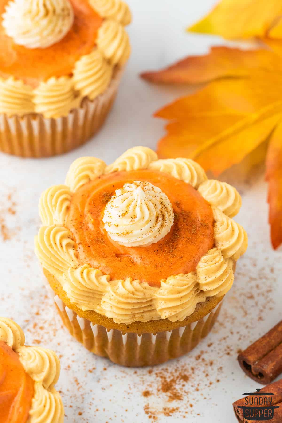 frosted pumpkin cupcakes up close next to a maple leaf