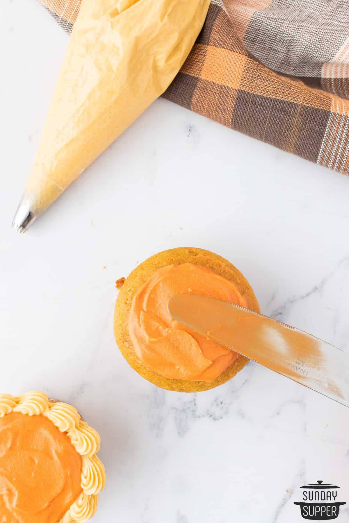 spreading orange cream cheese frosting onto the top of a cupcake with a knife