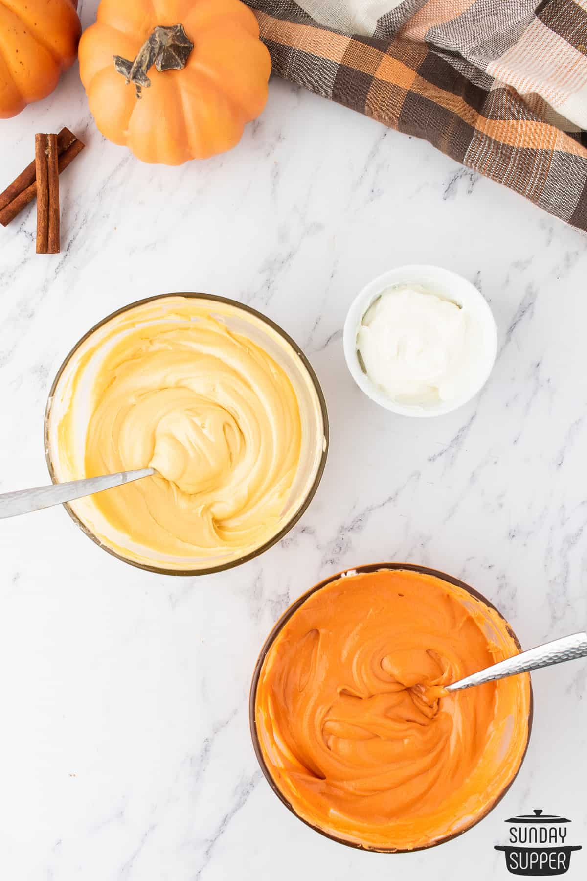 three bowls of cream cheese frosting: one is a brown-yellow to look like pie crust, the other is orange to look like pie filling