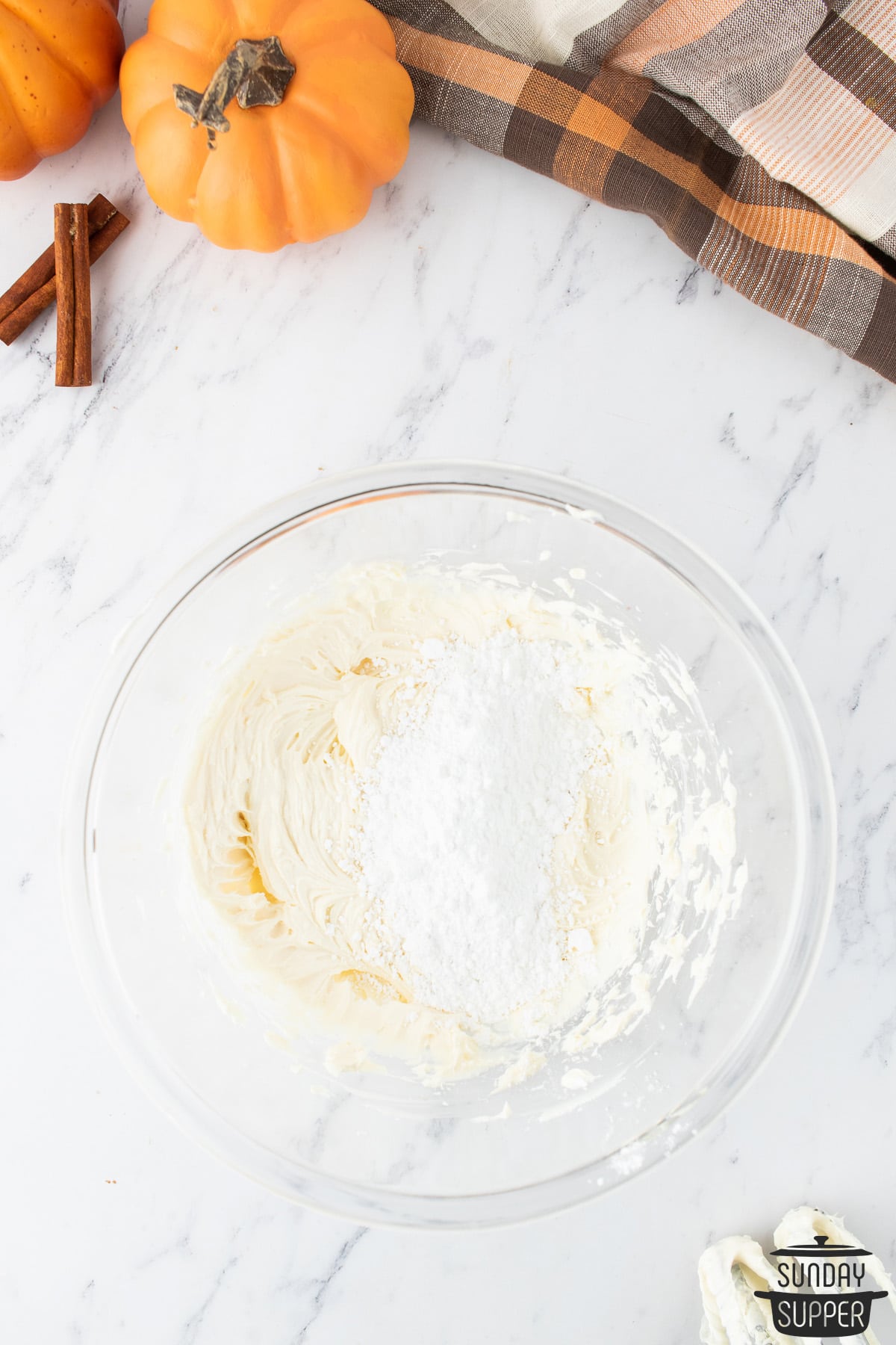 adding powdered sugar to cream cheese frosting in a bowl