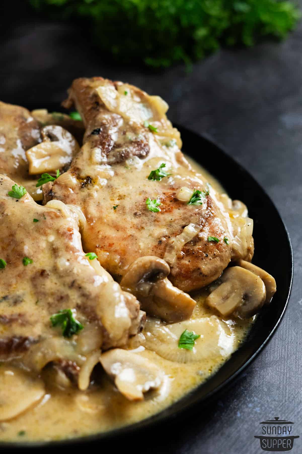 a big serving bowl filled with smothered pork chops, mushrooms, and gravy