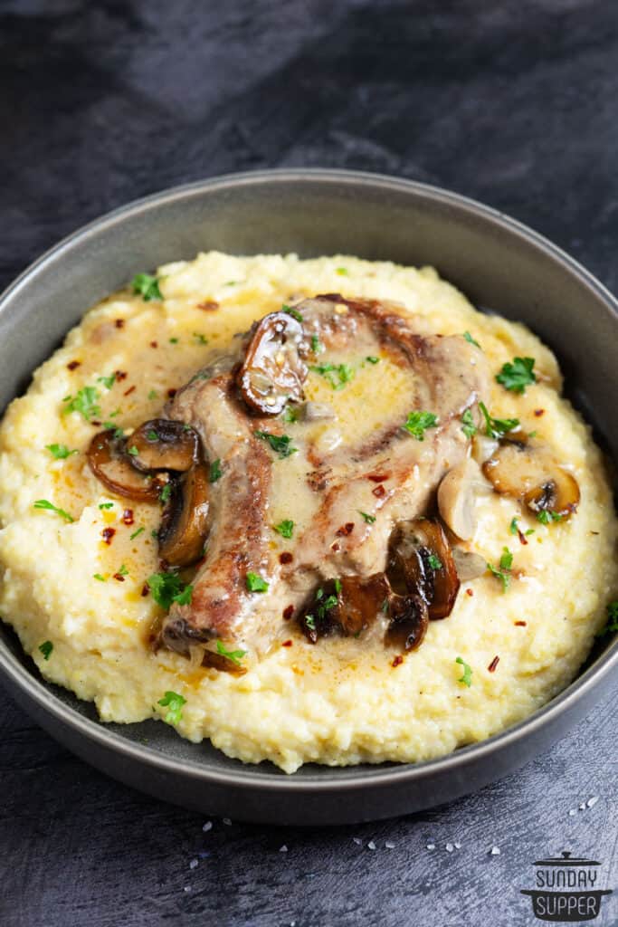 a bowl of mashed potatoes with a smothered pork chop on top